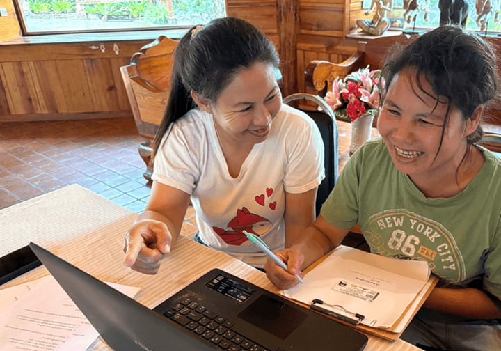 Two women sit at a laptop. 