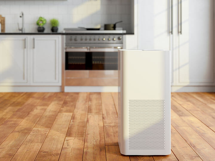 White room air purifier in a kitchen with white cabinets and wooden hardwood floors
